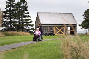A woman in a wheelchair and a friend on a gravel trail next to a picnic shelter