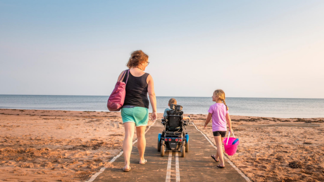 A mother and her two children, one in a wheelchair, go to the beach on a universal access mat..