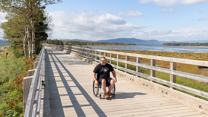 A man in a wheelchair on a boardwalk along a salted marsh.