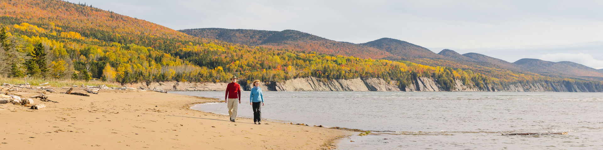 Un couple marche sur la plage de Penouille avec les montagnes colorés à l'arrière. 