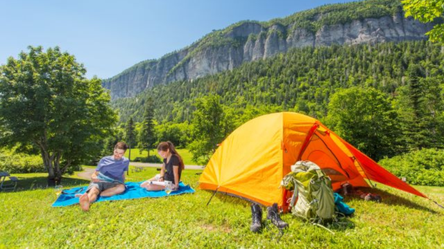 A couple of campers sitting on a blanket next to a tent are reading a visitor's guide. 