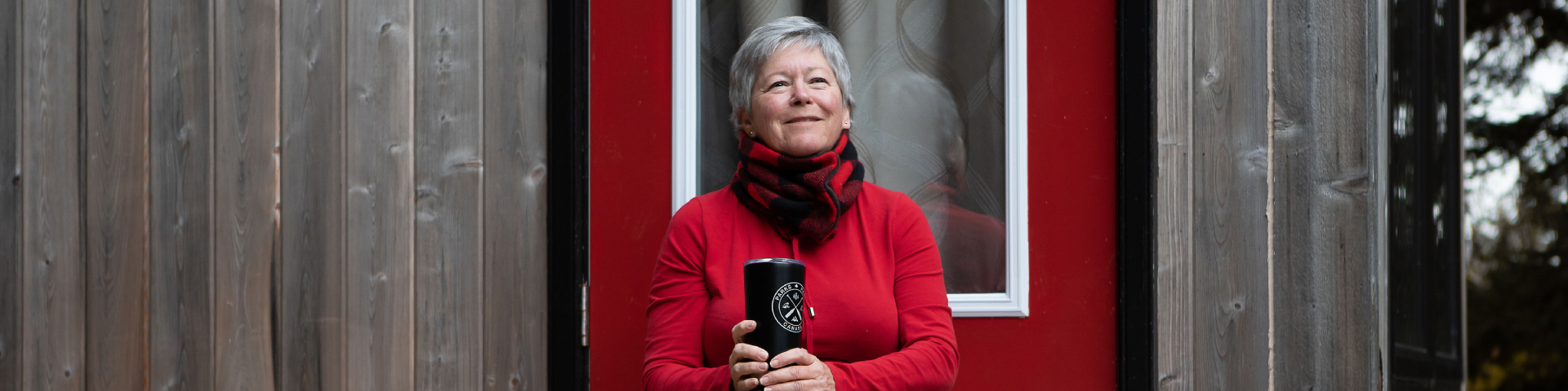 Une femme tout sourire tenant un thermos est assise sur le pas de la porte du microcube.