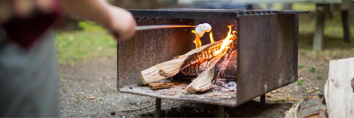 A camper roasts a marshmollow on a fire pit. 