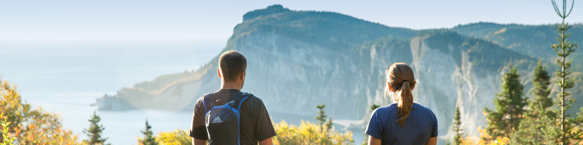 Deux randonneurs regardent un paysage de falaise et de mer le matin.