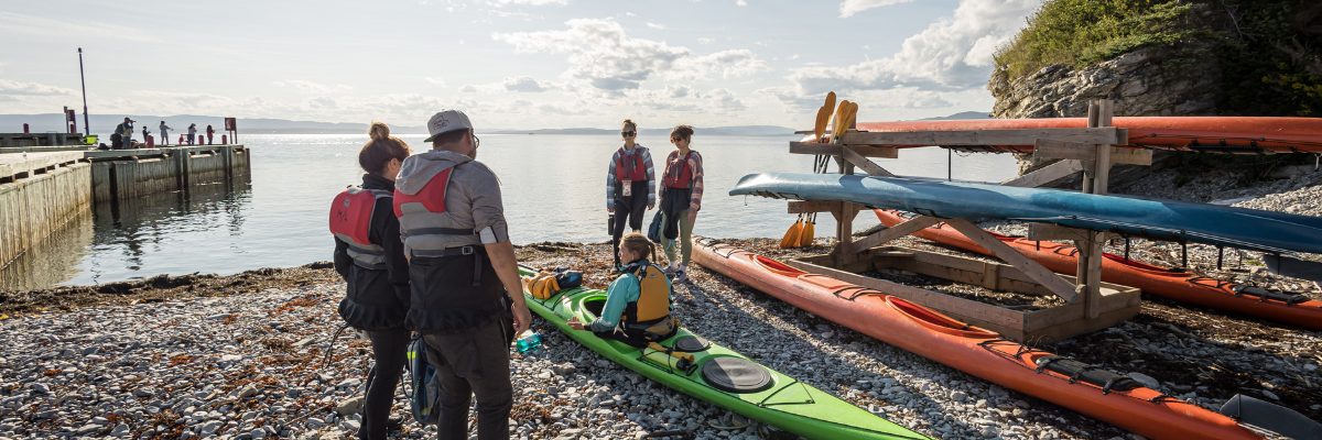 Visitors listen to the instructions of a kayak guide sitting in her kayak on the shore.