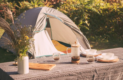 Accessoires de cuisine pour le camping sur une table, devant une tente, en nature.