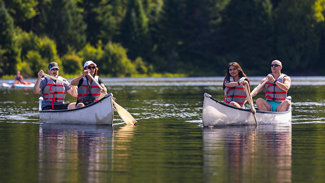 Deux couples de pagayeurs sont assis dans deux embarcations et font du canot sur un lac du parc national de la Mauricie lors d'une chaude journée d'été.