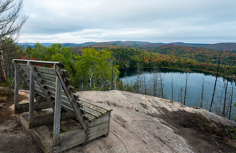 A wooden bench on a rock is facing a lake surrounded by hills.