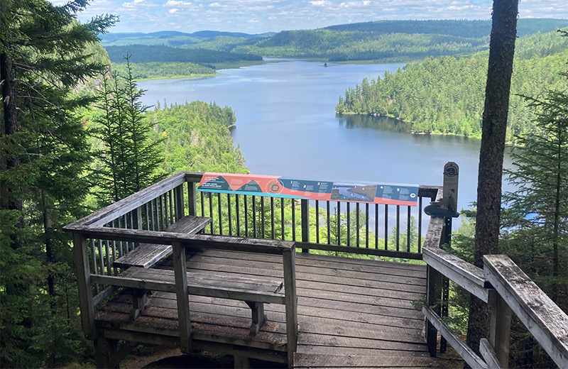 A wooden lookout with a view of a large lake surrounded by hills.
