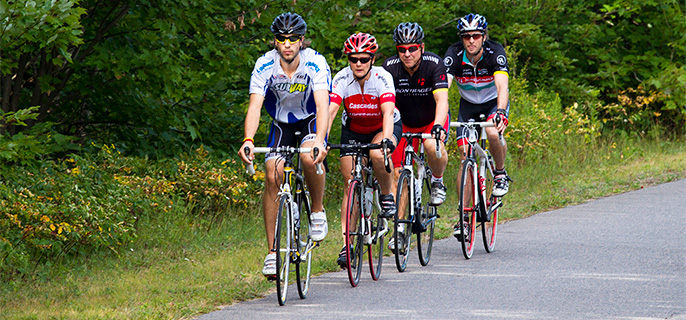 Quatre cyclistes qui roulent sur le bord de la route Promenade avec une forêt en arrière-plan.
