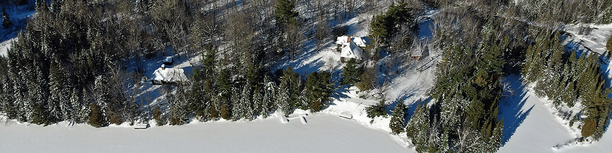 Two lodges, seen from the sky, located in the forest, in winter, on the edge of a lake.