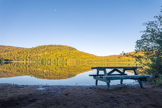 A picnic table on the beach with a lake and a forest in the background.