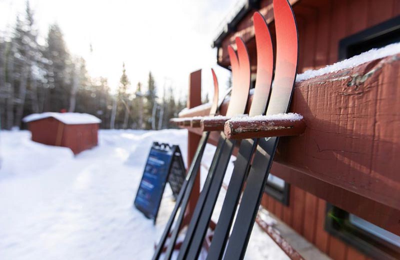 Des skis de fond sont accrochés sur un support en bois à l'extérieur d'un bâtiment, en hiver.