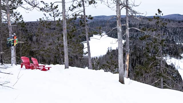 Des chaises rouges dans la forêt enneigée avec un magnifique paysage composé de lacs et d'arbres.