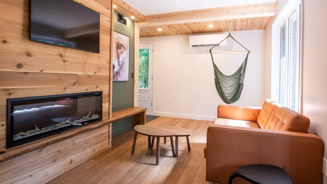 Un salon décoré de bois et illuminé où se trouvent un hamac, de petites tables, un foyer, une télévision et un cadre de renard.