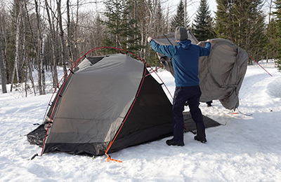 A person is fixing a tent in the snow.