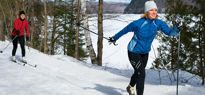 Two women cross-country skiing on a trail by the lake.
