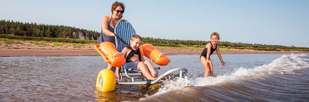 Une famille joue dans les vagues, dont un enfant sur un fauteuil roulant de plage