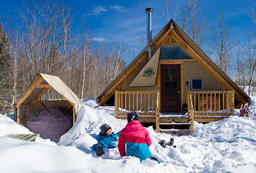 Deux enfants jouent dans la neige devant une tente oTENTik