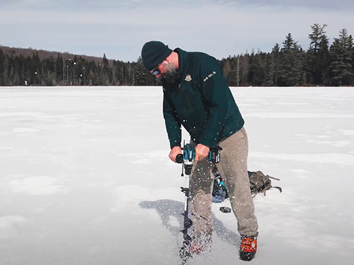 Parks Canada worker digs a hole in the ice on a lake