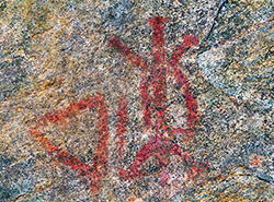 Des peintures rupestre sur du granit représentant une tortue et un triangle rouges