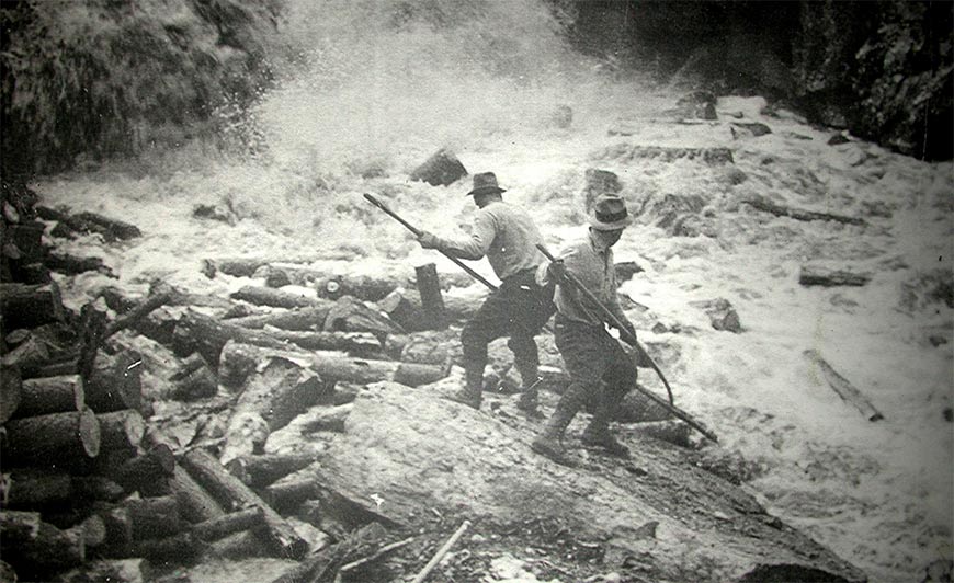 Two log drivers at work at the base of a waterfall.