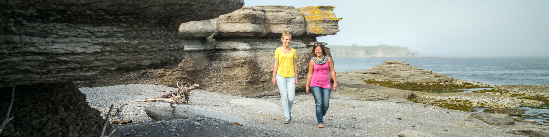 Une femme et sa fille marchent sur le littoral, près de monolithes.