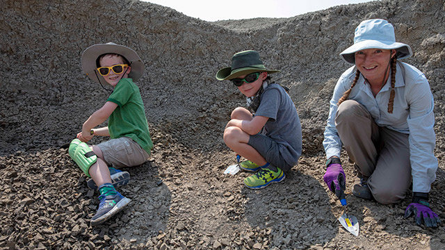 Deux garçons creusent des fossiles avec le paléontologue.