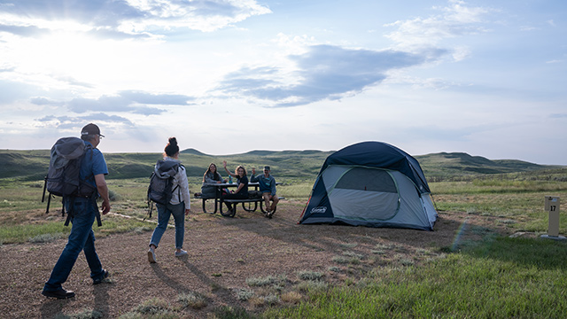 Deux visiteurs s'approchent d'un groupe assis à une table de pique-nique dans un emplacement de camping du terrain de camping Rock Creek.