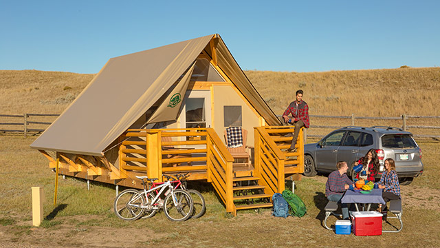 Un groupe de jeunes adultes savoure leur petit-déjeuner à l'extérieur de leur abri oTENTik de Parcs Canada au camping de la Vallée-de-la-Frenchman, dans le parc national des Prairies.