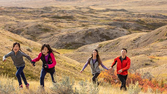 Deux enfants montant une colline en courant, suivis de leurs parents, avec en arrière-plan le paysage du bloc Ouest du parc national des Prairies