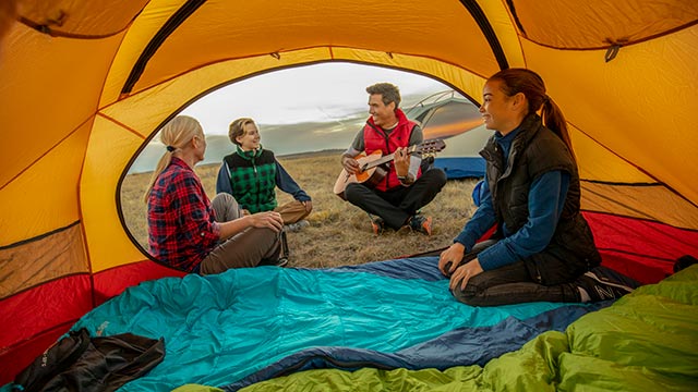 View from inside a tent looking out, of four campers sitting outside their tents, while one plays guitar, in the West Block of Grasslands National Park