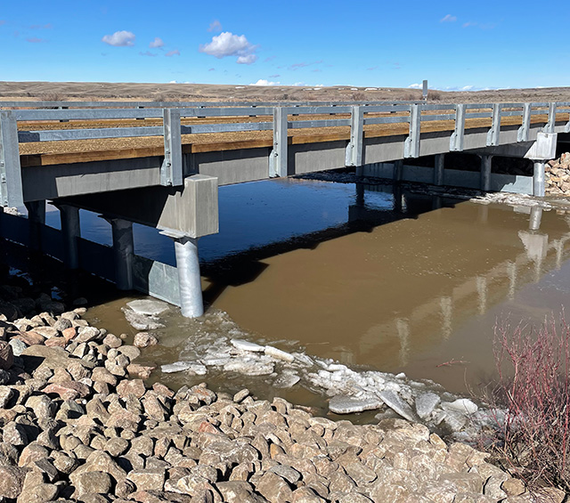 Water and ice of river flowing beneath steel and concrete bridge. 