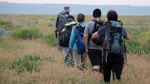 Visitors wearing backpacks and snake gaiters follow a Parks Canada staff member. 
