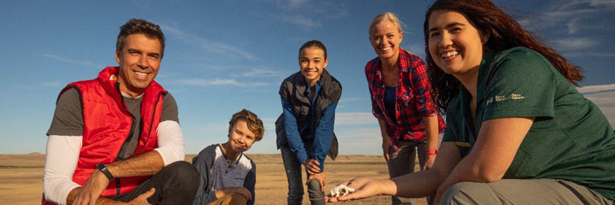 Un interprète au parc national des Prairies montre des accessoires éducatifs à une famille sur les lieux d’une colonie de chiens de prairie.