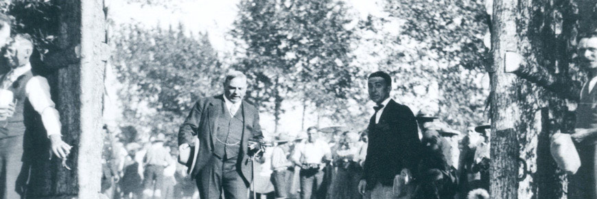 Photo historique du Premier ministre William Lyon McKenzie King en habit passant entre deux portes en bois devant un groupe d’adultes