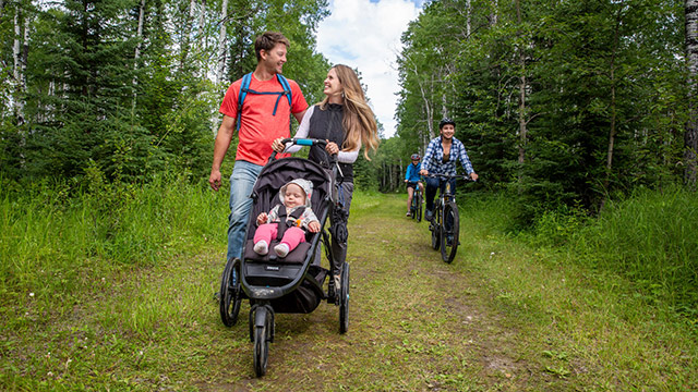 A couple walk with their infant in a stroller on the Red Deer Trail/ Fisher Trail as visitors bike by them in Prince Albert National Park.