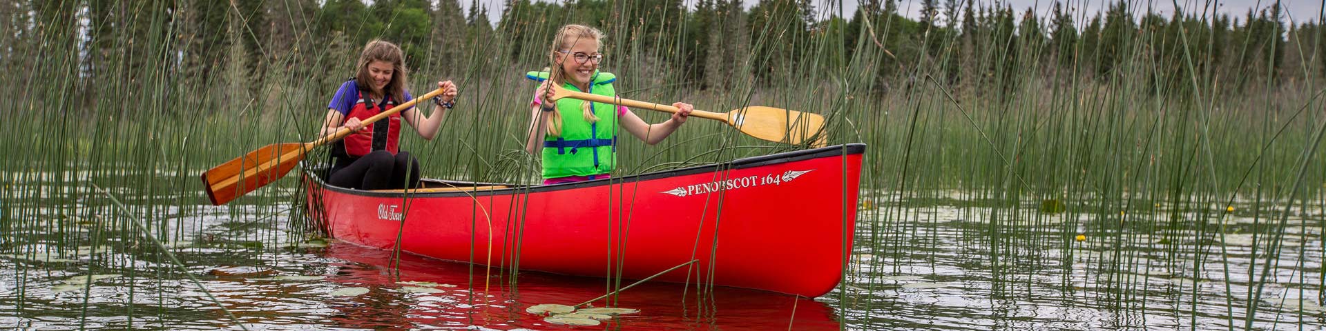 Girls paddle a canoe on Waskesiu River during the summer in Prince Albert National Park.