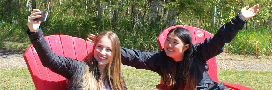 Deux jeunes femmes prennent une autophoto, assises dans des chaises rouges de Parcs Canada.