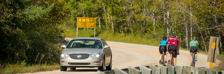 A car passes a group of cyclists on a scenic highway.