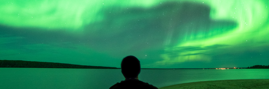 La silhouette de la tête et des épaules d’un homme qui observe le ciel nocturne se détache sur un fond d’aurore boréale.