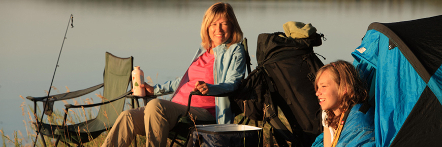 Une femme et sa fille admirent le lever du soleil depuis leur emplacement de camping au bord d’un lac.