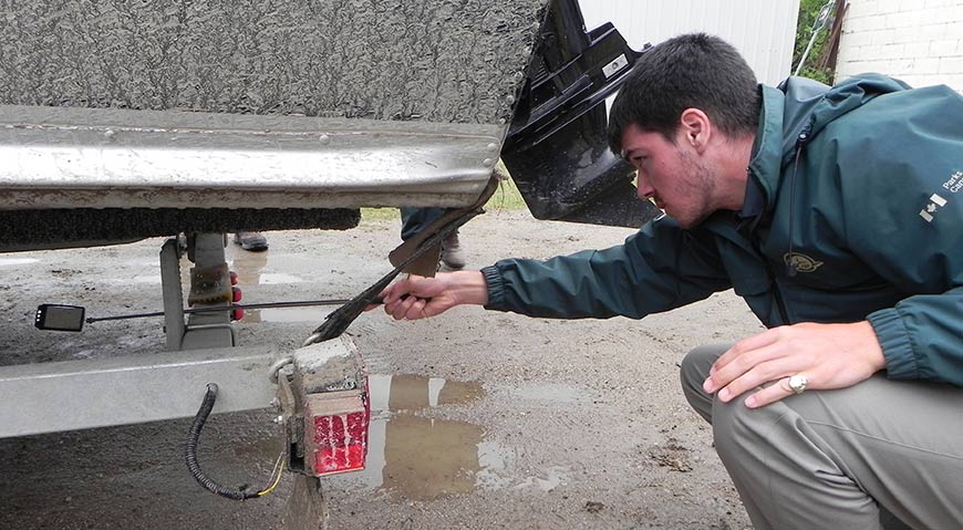 A park employee inspects the back of a boat and the accumulated debris on the back of the boat trailer. 