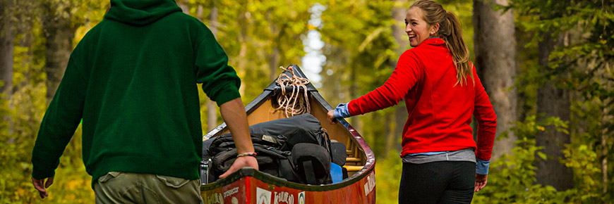 A young woman smiles at a man as they push their loaded canoe along the rail car portage at Kingsmere Lake.