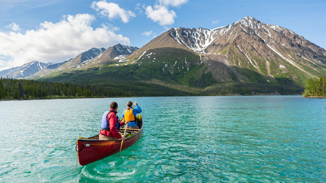 People paddling in a canoe on a blue lake and a mountain ahead of them