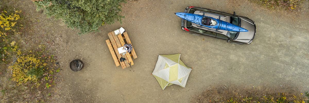 Un emplacement de camping avec une tente, une voiture, une table de pique-nique et un foyer.