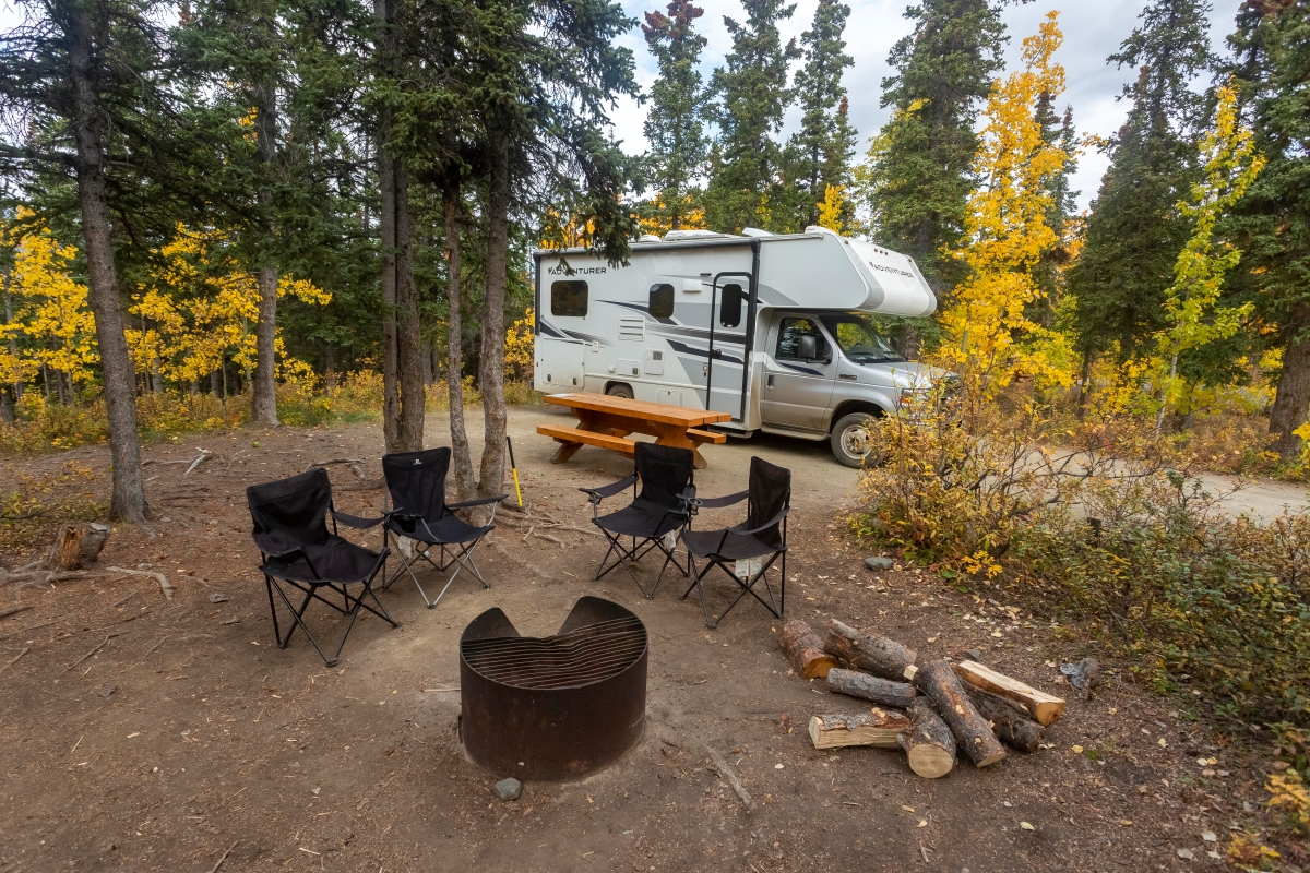 A recreational vehicle parked beside a campsite cleared of all items except for furniture.