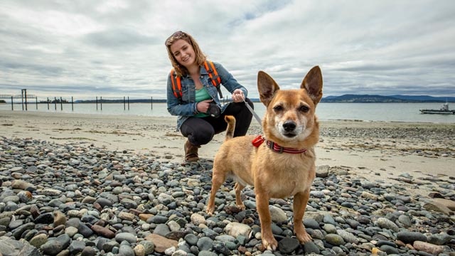 A young woman holds her dog on leash at Sidney Spit. 