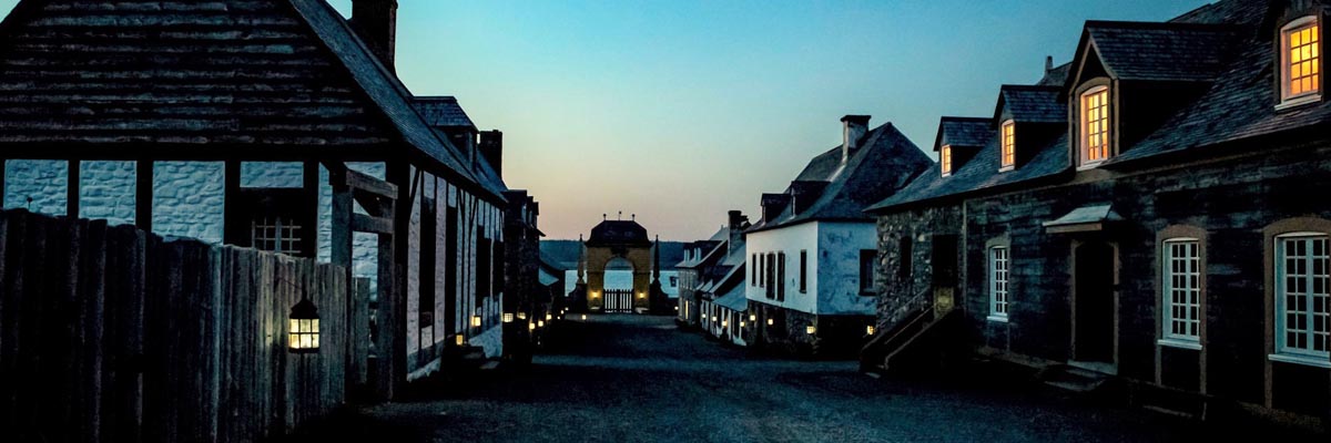 The lower town area of the Fortress of Louisbourg is lit by lantern light on a clear evening. 