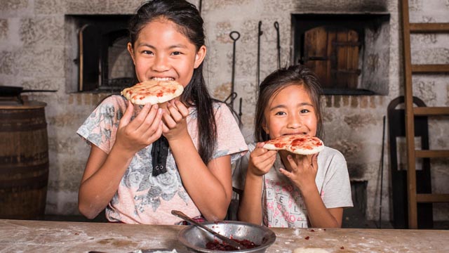 Visitors take a bite of freshly-baked bannock in the Bake House. Lower Fort Garry National Historic Site.